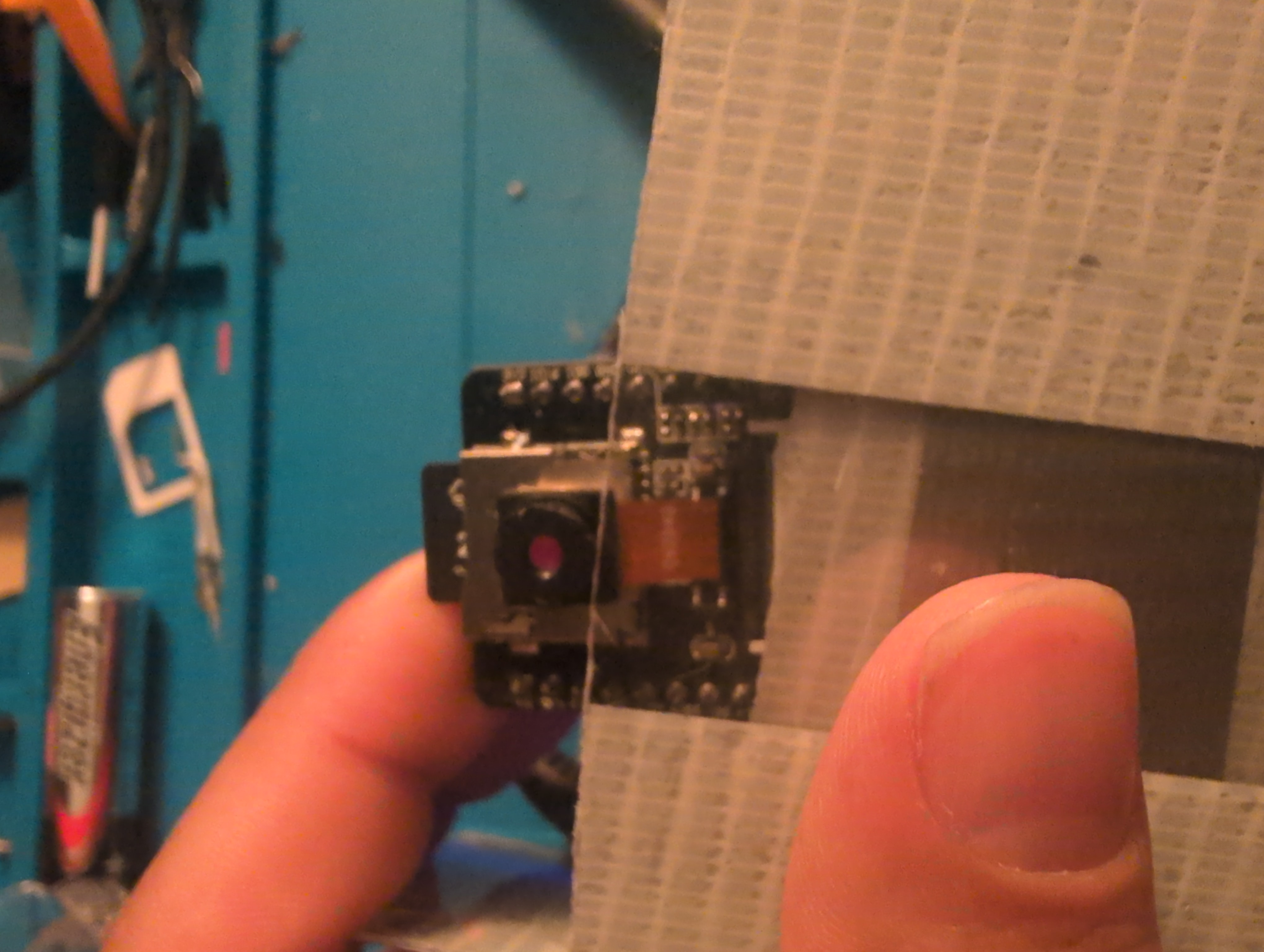 Close-up of Roberto Vega’s physical camera prototype mounted in a temporary bench fixture, with the camera lens and ribbon cable visible.